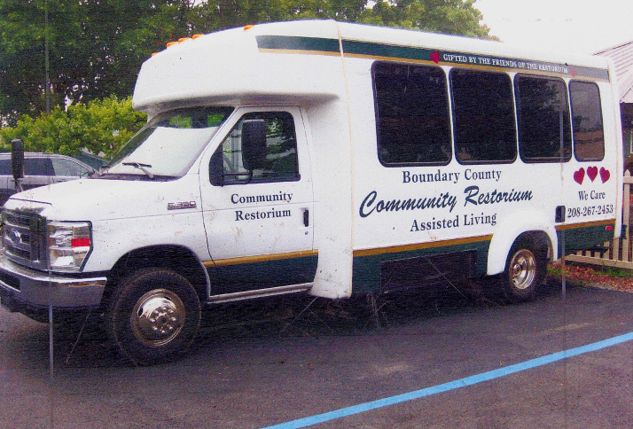 A white shuttle van labeled "Boundary County Community Restorium Assisted Living" is parked in a lot. The van displays public service info, including a phone number and Boundary County ID, printed on the side. | Boundary County ID
